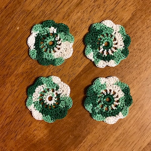 May include: Four crocheted doilies in shades of green and white. Each doily has a circular design with a center hole.