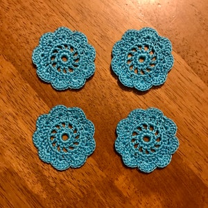 May include: Four teal blue crocheted doilies with a spiral design in the center.