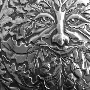 May include: A silver metal sculpture of a Green Man with a face surrounded by oak leaves and acorns.