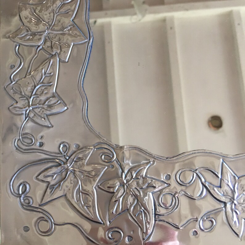 May include: A silver-colored, decorative picture frame with embossed leaf and vine designs. The frame has a wavy edge and features detailed botanical patterns, adding a touch of nature-inspired elegance to home decor.
