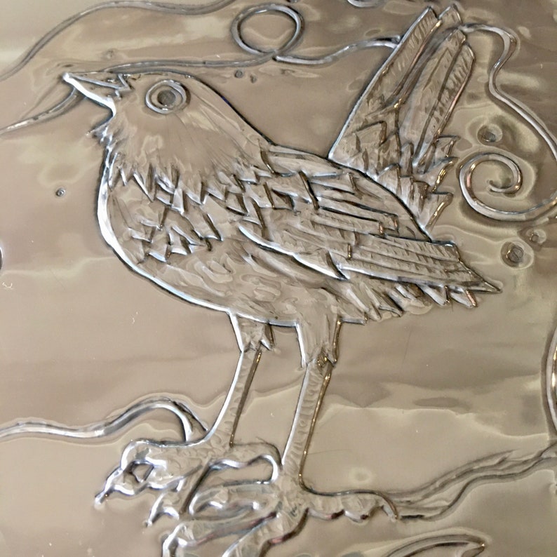 May include: A detailed, silver-colored relief of a bird perched on a branch. The bird is depicted with intricate feather details and stands out against the textured background. The artwork showcases a nature-inspired theme.