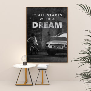 May include: Black and white photograph print of a child riding a bicycle in front of a classic car with the text "It all starts with a dream" above the image.