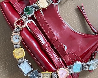 May include: A red leather handbag with a chain strap and multiple silver and gold wristwatches attached to it. The watches are in various shapes and sizes, including square, round, and heart-shaped.