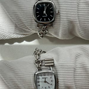May include: Two silver watches with chain link bands. The top watch has a black face with silver hands and the text "QUARTZ". The bottom watch has a white face with black hands and the text "Meidiors".