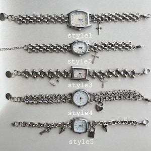 May include: Five silver wristwatches with different chain styles and charms. The charms include a cross, a music note, a heart, a key, and a padlock. The watches have white faces and black Roman numeral markings.
