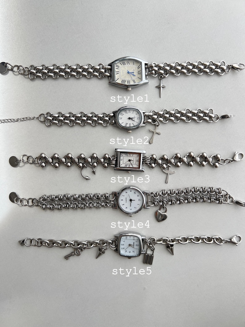 May include: Five silver wristwatches with different chain styles and charms. The charms include a cross, a music note, a heart, a key, and a padlock. The watches have white faces and black Roman numeral markings.