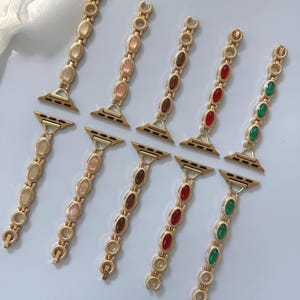 May include: Gold-toned watch bands with oval-shaped gemstones in various colors, including yellow, pink, brown, red, and green. The bands are designed to attach to a smartwatch and feature a decorative chain-link style.