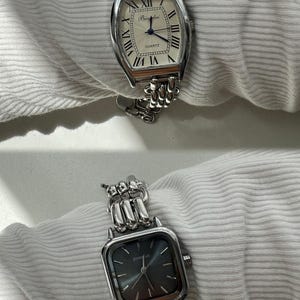 May include: Two silver watches with chain link bands. The top watch has a white face with black Roman numeral hour markers and the text "QUARTZ". The bottom watch has a black face with silver hands and the text "TEMSIAN".