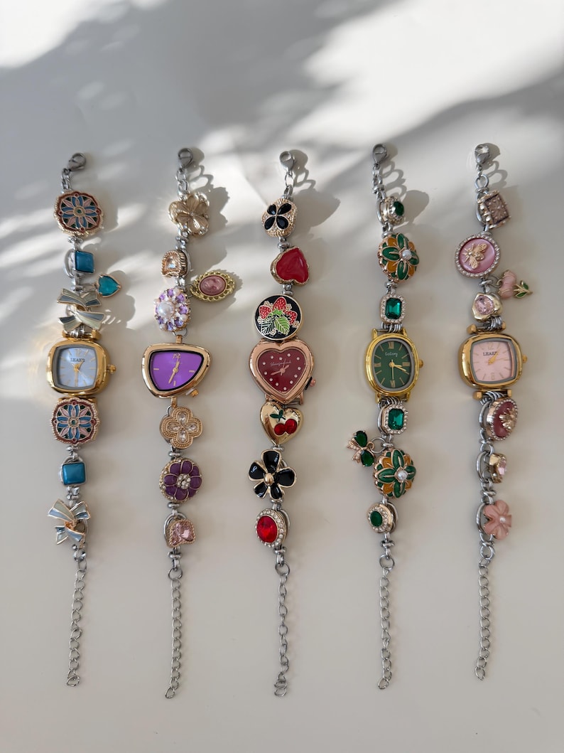 May include: Five decorative watch bracelets with various charms and watch faces. The bracelets feature a mix of floral, heart, and gemstone designs in gold, silver, red, green, and purple. Each bracelet has a chain extension.