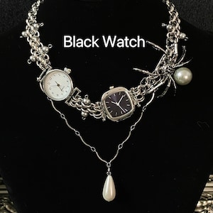 May include: A silver necklace with two watches, one with a black face and one with a white face. The necklace also features a spider charm and a pearl pendant.