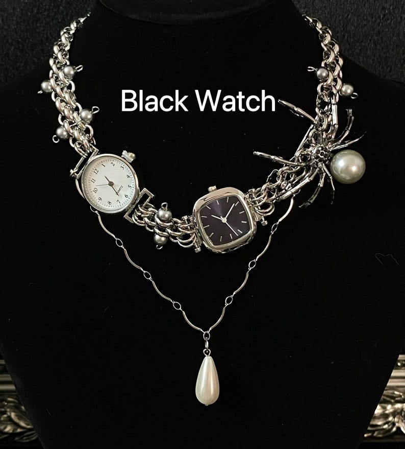 May include: A silver necklace with two watches, one with a black face and one with a white face. The necklace also features a spider charm and a pearl pendant.