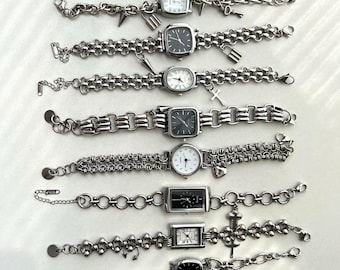 May include: A collection of ten silver-toned wristwatches arranged in rows. Each watch features a unique metal link bracelet, some adorned with small charms like keys, locks, crosses, or stars. The watch faces vary in shape and dial colour.