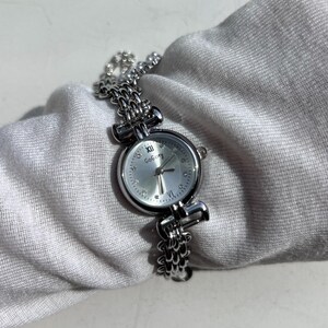 May include: A silver-toned wristwatch with a chain-link band and a round face. The watch face is silver with Roman numeral hour markers and the brand name "GoBoey". The watch is displayed on a white fabric surface.