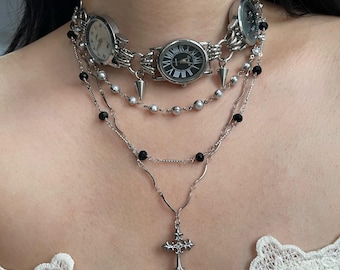 May include: A silver choker necklace with three attached watch faces and a silver chain with black beads. A silver chain with a silver cross pendant hangs below.