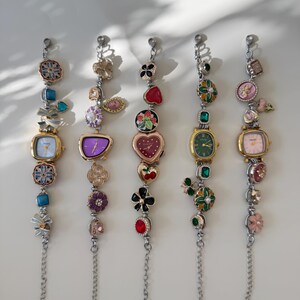 May include: Five decorative charm bracelets with watch faces. Each bracelet has a silver chain and various colourful charms, including flowers, hearts, and gemstones. The watch faces have different shapes and colours, with gold-tone metal cases.
