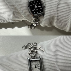 May include: Two silver watches with square faces and chain link bands. The top watch has a black face with white hands and the text "RATE QUARTZ". The bottom watch has a white face with black Roman numeral markings and black hands.