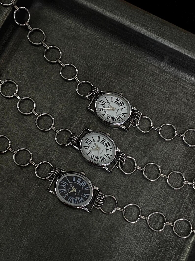 May include: Three silver watches with Roman numeral faces attached to a silver chain with large, round links.