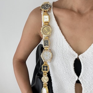 Puede incluir: Una original correa para el hombro hecha de varios relojes vintage dorados. Los relojes tienen diferentes formas y diseños de esfera, creando un accesorio elegante y llamativo. La correa está sujeta a un bolso negro.