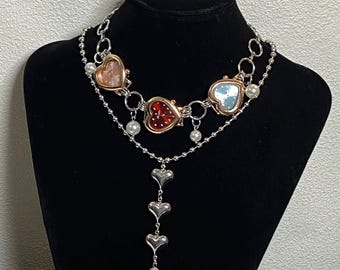 May include: A silver chain necklace with four heart-shaped watch pendants. The pendants are red, pink, blue, and white. The necklace also has a silver chain with three heart-shaped charms hanging from it.