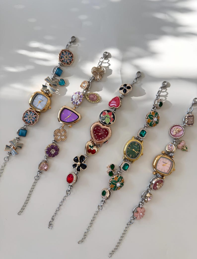 May include: Five decorative bracelet watches with various colourful embellishments. Each watch features a different face shape and colour, including square, oval, and heart-shaped designs. The bracelets are adorned with floral, gemstone, and charm accents.