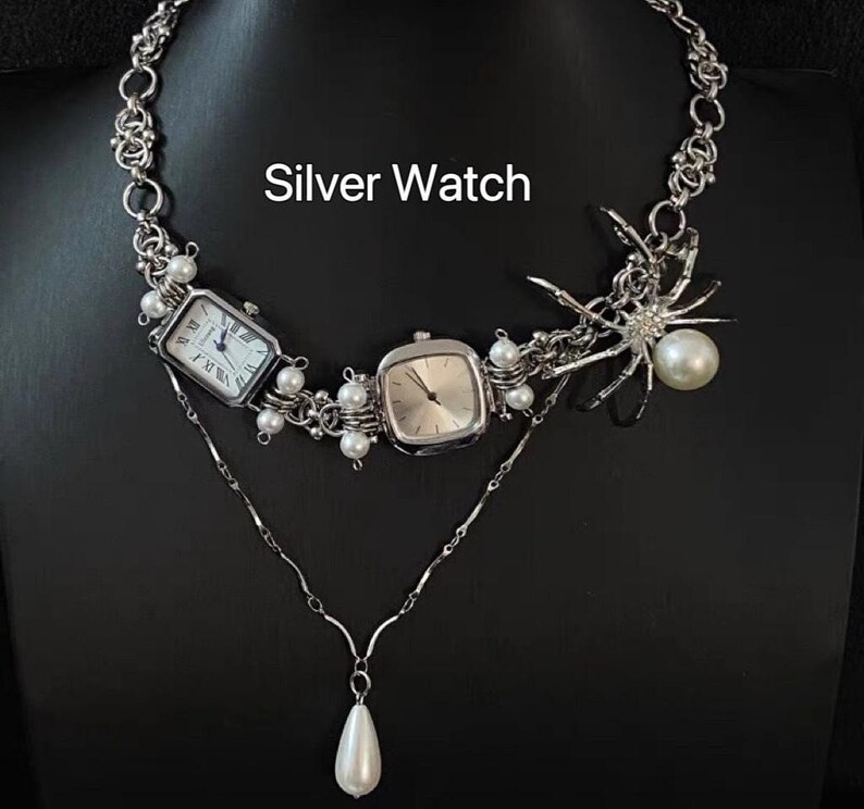 May include: A silver chain necklace with two silver watches and a silver spider charm. The necklace has white pearl accents.