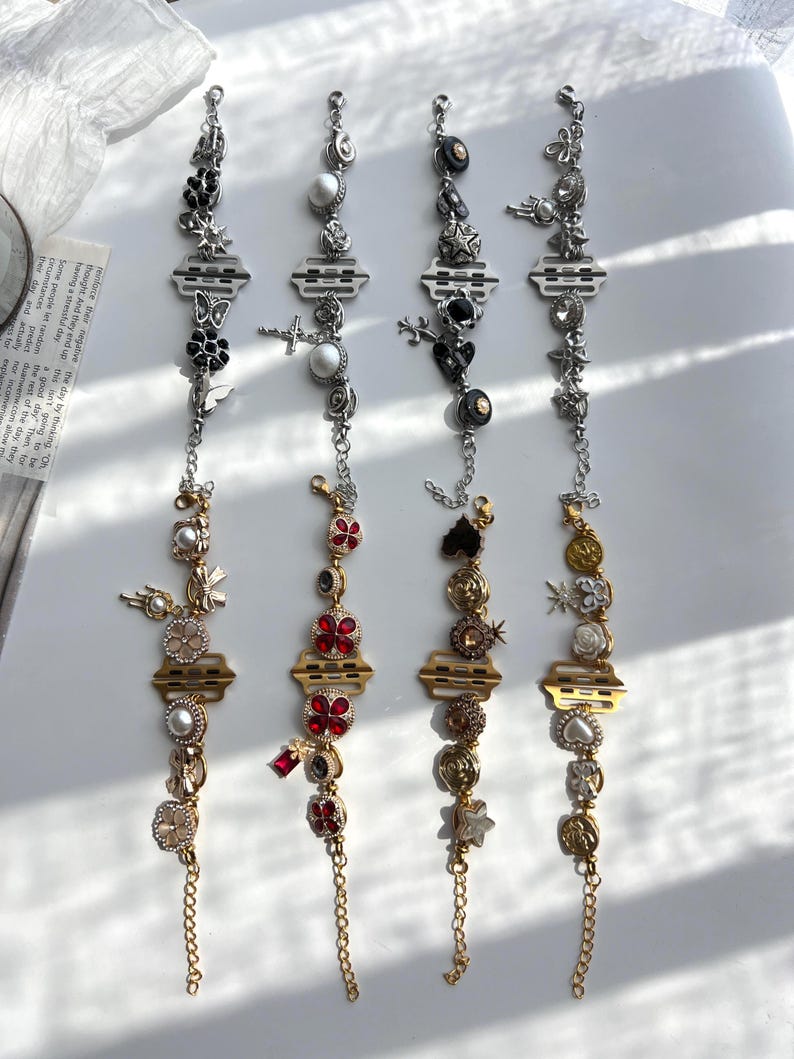 May include: Four decorative bracelets with various charms, including crosses, stars, and flowers. The bracelets feature silver and gold chains, with accents of black, red, and white. The charms are detailed and ornate.