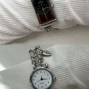 May include: Two silver wristwatches with chain link bands. The top watch has a black face with the word "GoGory" printed on it. The bottom watch has a white face with black numbers and hands and the word "QUARTZ" printed on it.