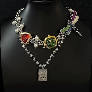 May include: A silver chain necklace with a heart-shaped watch, a square watch with a green face, a dragonfly charm, and a locket with a tree design.