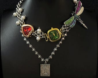 May include: A silver chain necklace with a heart-shaped watch, a square watch with a green face, a dragonfly charm, and a locket with a tree design.