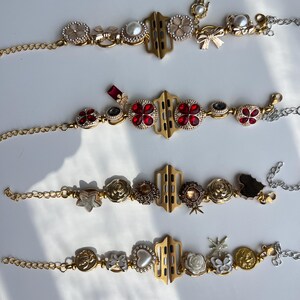 May include: Four decorative watch bands with gold and silver chains. Each band features a gold-colored central connector and is adorned with various embellishments, including pearls, red gems, and floral designs. The bands are displayed on a white surface.