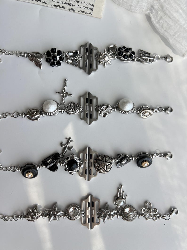 May include: Four silver-toned bracelets with various decorative charms. Charms include black flowers, butterflies, stars, crosses, and round white stones. Each bracelet has a central rectangular clasp and a chain link band.