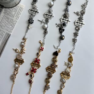 May include: Four decorative bracelets with various charms, including flowers, stars, and geometric shapes. The bracelets feature silver and gold chains with a variety of colors, including red, black, and white. The bracelets are displayed on a white surface.