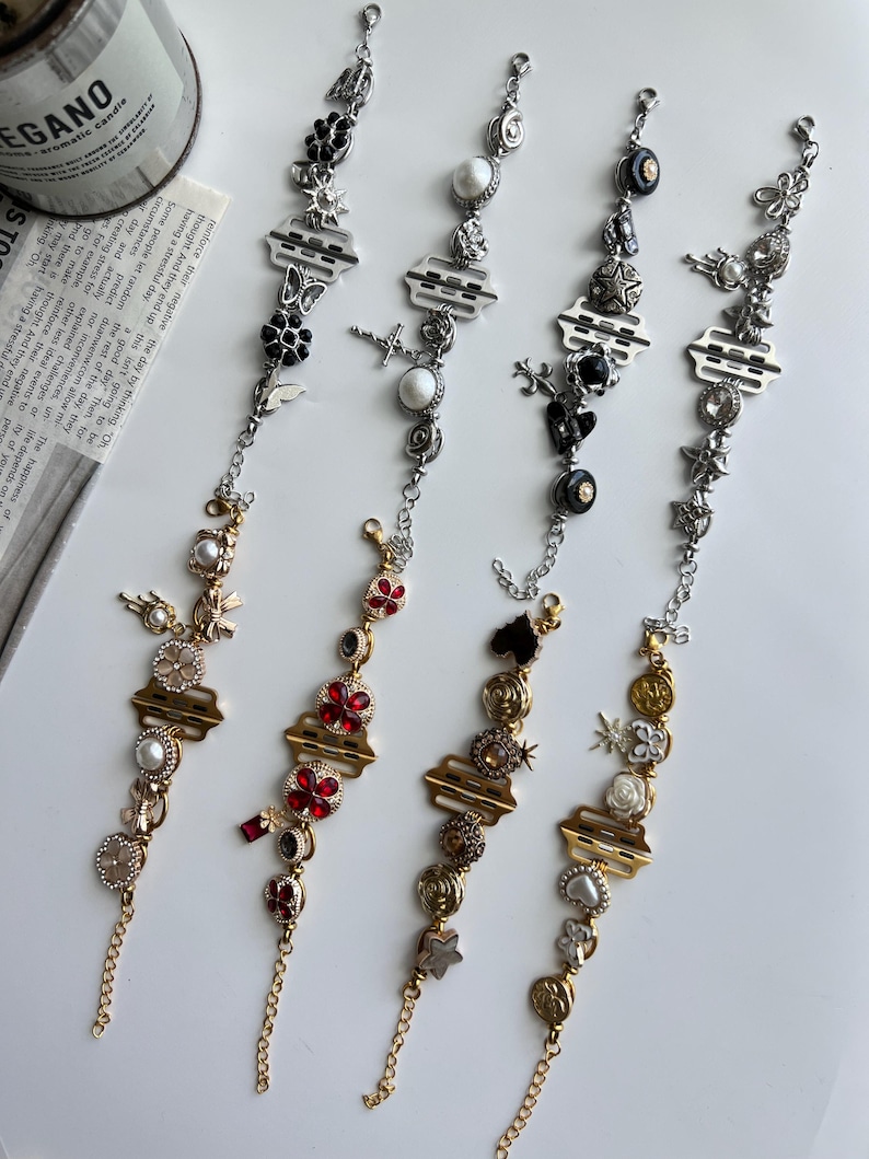 May include: Four decorative bracelets with various charms, including flowers, stars, and geometric shapes. The bracelets feature silver and gold chains with a variety of colors, including red, black, and white. The bracelets are displayed on a white surface.