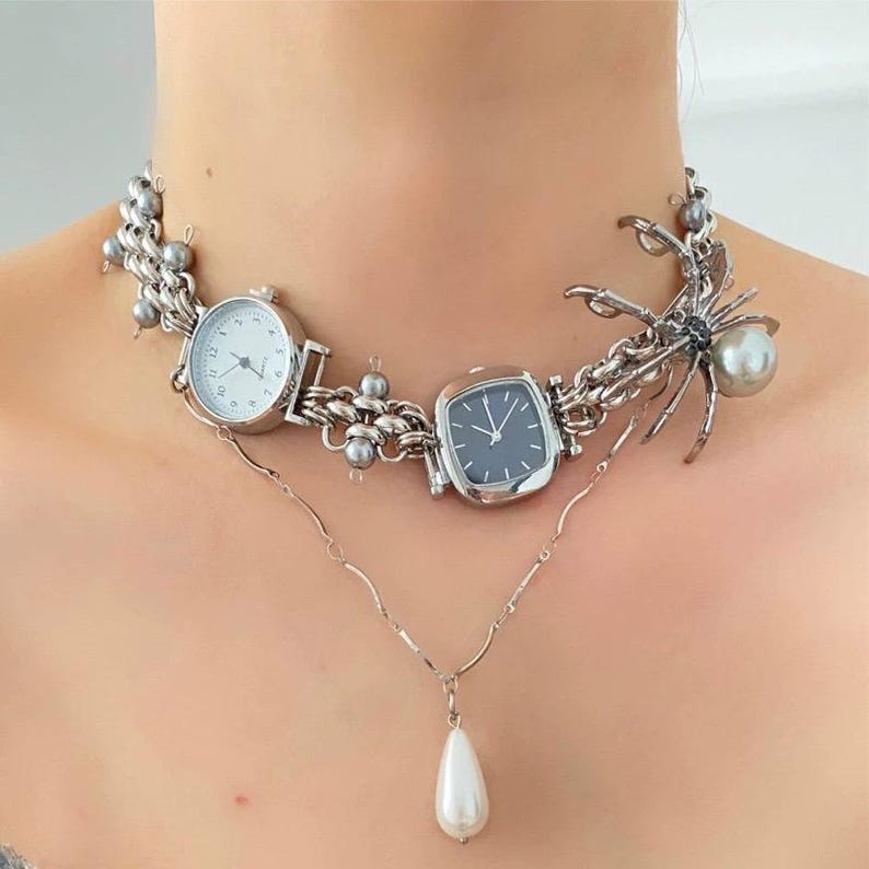 May include: A silver necklace with three silver watches and a silver spider charm with a pearl. The necklace also has a pearl pendant.