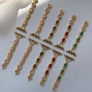 May include: Gold-toned watch bands with oval-shaped gemstones in various colors, including cream, pink, brown, red, and green. The bands are designed with a chain-like structure and are displayed on a light-colored surface.