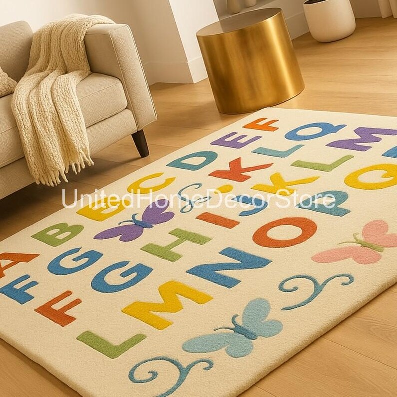 K&ouml;nnte beinhalten: Ein rechteckiger cremefarbener Teppich mit dem Alphabet in verschiedenen Farben. Die Buchstaben sind gro&szlig; geschrieben und in einer verspielten Schriftart gehalten. Auf dem Teppich sind Schmetterlinge in Blau, Lila und Rosa verstreut. Der Teppich liegt auf einem Holzboden.