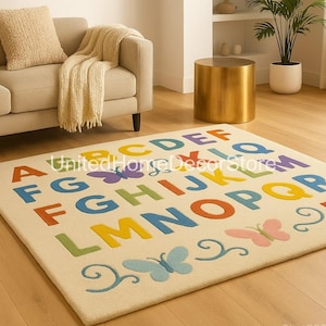 K&ouml;nnte beinhalten: Ein rechteckiger cremefarbener Teppich mit dem Alphabet in verschiedenen Farben. Der Teppich zeigt Schmetterlinge und den Text "United Home Decor Store". Der Teppich liegt auf einem Holzboden, mit einem Sofa und einem Beistelltisch im Hintergrund.