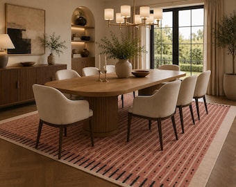Könnte beinhalten: Ein Esszimmer mit einem ovalen Holztisch und acht gepolsterten Stühlen. Unter dem Tisch liegt ein gemusterter Teppich in Rosa- und Cremetönen. Über dem Tisch hängt ein Kronleuchter, und ein großes Fenster bietet einen Blick auf den Garten.
