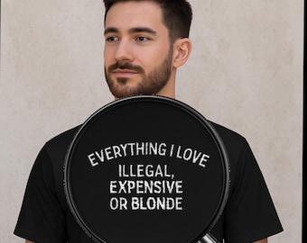 May include: Black t-shirt with the white text "EVERYTHING I LOVE, ILLEGAL, EXPENSIVE OR BLONDE." The shirt is a crew neck style and appears to be made of a soft material. The text is centered on the chest.