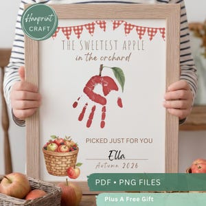 May include: A framed print featuring a red handprint shaped like an apple, with the text THE SWEETEST APPLE in the orchard, PICKED JUST FOR YOU, Ella, and Autumn 2026. The design includes red gingham bunting and a basket of apples.