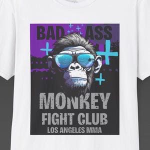 May include: White t-shirt with a graphic of a monkey wearing sunglasses. The text reads "BAD ASS MONKEY FIGHT CLUB LOS ANGELES MMA". The design incorporates purple and blue colours.