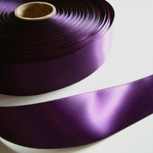 May include: A roll of deep purple satin ribbon. The ribbon is wound tightly and has a smooth, shiny finish.