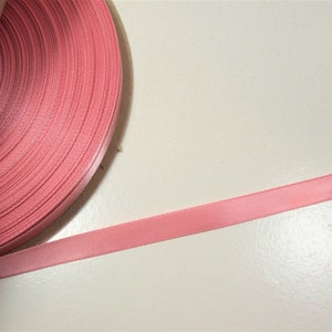 May include: A roll of pale pink satin ribbon. The ribbon is a solid colour and is unwinding from a cardboard core. The ribbon is smooth and has a slight sheen, suitable for crafts and gift wrapping. The ribbon's width is approximately 1 cm.