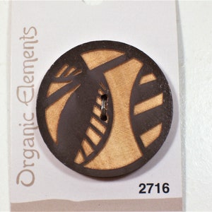 May include: A circular wooden button featuring a dark brown laser-cut geometric pattern over a light tan wood grain base. The button is attached to a white display card labeled Organic Elements with the number 2716 printed in the bottom corner.