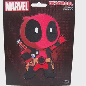 Puede incluir: Un parche de aplique de Deadpool en una tarjeta negra con el logo de Marvel. El parche presenta un Deadpool de dibujos animados en rojo y negro con una espada. La tarjeta también tiene el texto "DEADPOOL APPLIQUE APLICACIÓN".