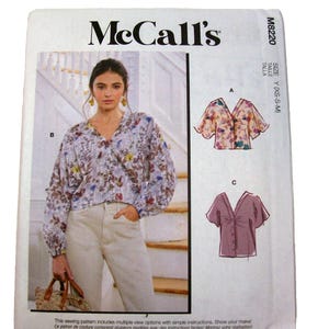 May include: McCall's M8220 sewing pattern envelope featuring a V-neck blouse with long sleeves and a floral print. The pattern includes three variations labeled A, B, and C, showing a cropped floral top, a solid-colored top, and a long-sleeved blouse.
