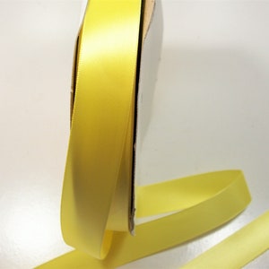 May include: A roll of bright yellow satin ribbon. The ribbon is unwound, showing a smooth, glossy texture. The ribbon is a solid, sunny yellow colour, ideal for crafts, gift wrapping, or decorative purposes.
