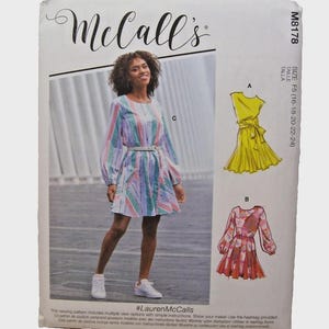 May include: McCall's M8178 sewing pattern envelope featuring a dress with long sleeves and a belted waist in a multi-coloured striped fabric. The package displays illustrations of two additional dress variations, one in solid yellow and one in a floral print.