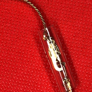 May include: A gold-colored twisted metal chain with a clear plastic tube clasp. The clasp has a gold-colored metal piece with a decorative design.