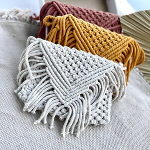 Macrame handwoven purses in a row one behind another-beige, mustard yellow, brownz Placed upright on plain beige fabric.